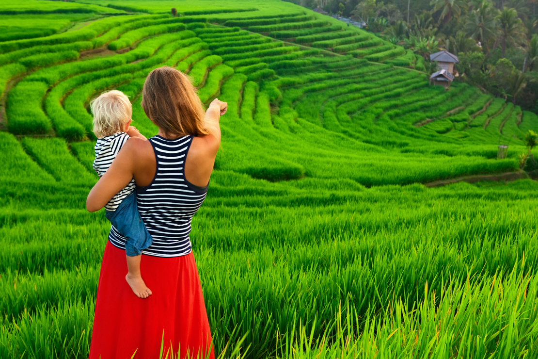 shutterstock_567711667 Beautiful view of Balinese traditional fields. Nature walk in green rice terrace. Happy mother hold happy little baby traveler. Travel adventure with child, family summer vacation in.jpg