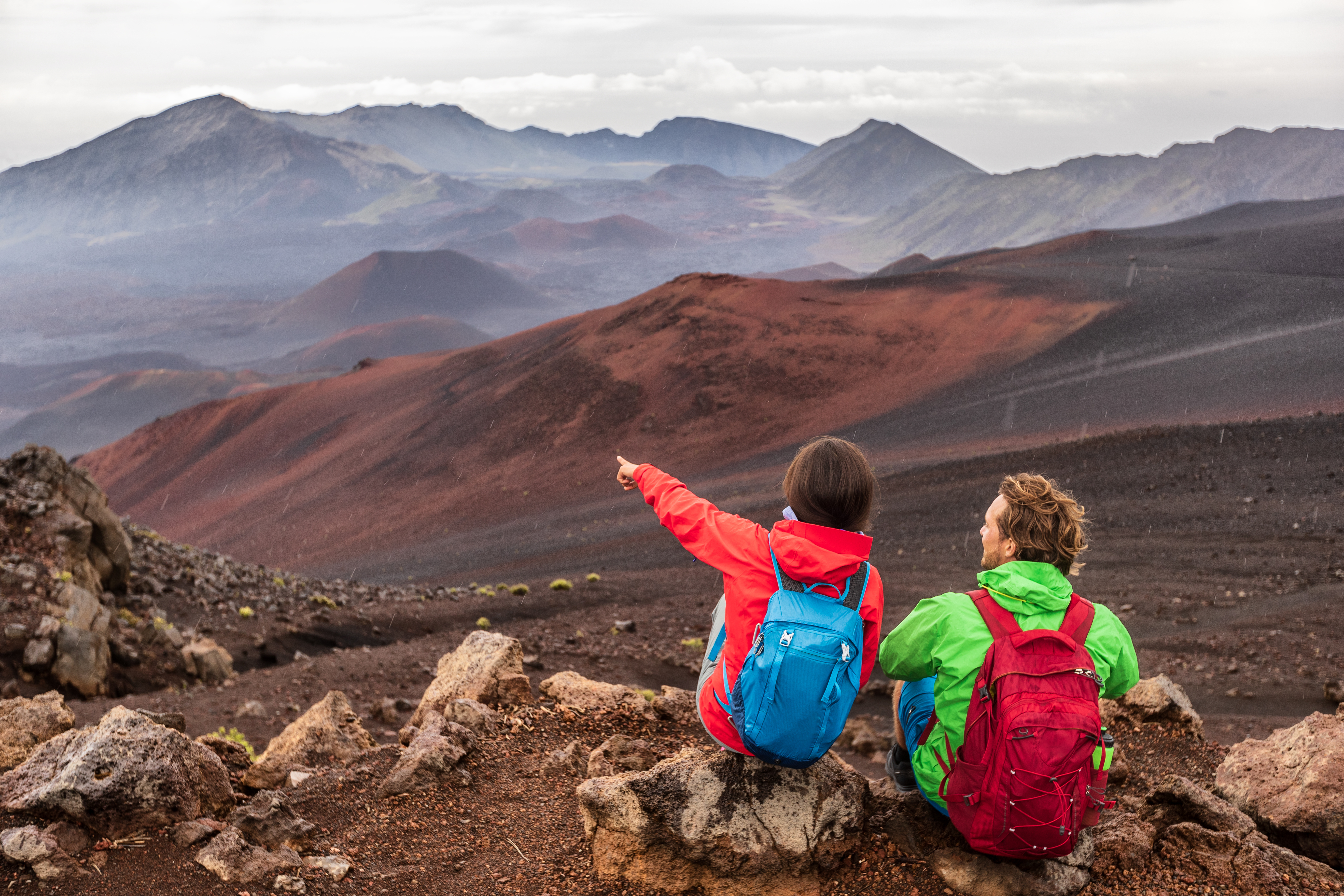 Hiking travel vacation in Maui volcano, Hawaii. USA travel woman with backpack pointing at Haleakala volcano landscape. Couple tourists resting outdoors. - Billede.jpg