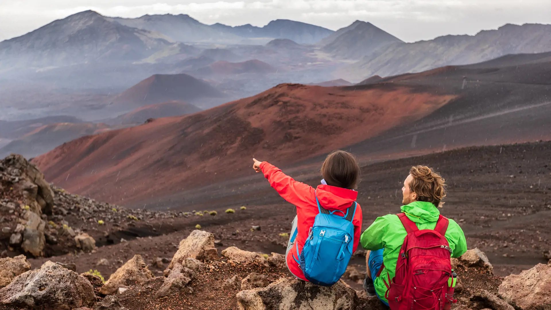 Hiking travel vacation in Maui volcano, Hawaii. USA travel woman with backpack pointing at Haleakala volcano landscape. Couple tourists resting outdoors. - Billede.jpg