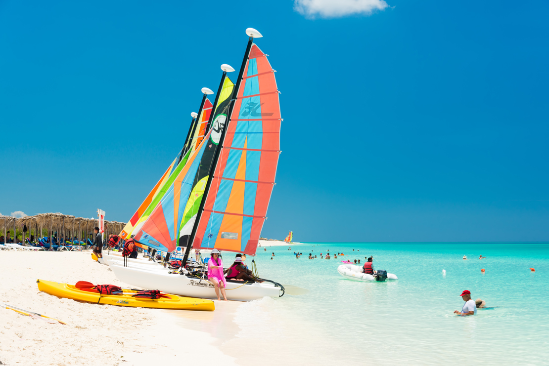 shutterstock_207668812 CAYO SANTA MARIA, CUBA - JULY 16, 2014  Tourists enjoy the beautiful beach with colorful sailboats.jpg