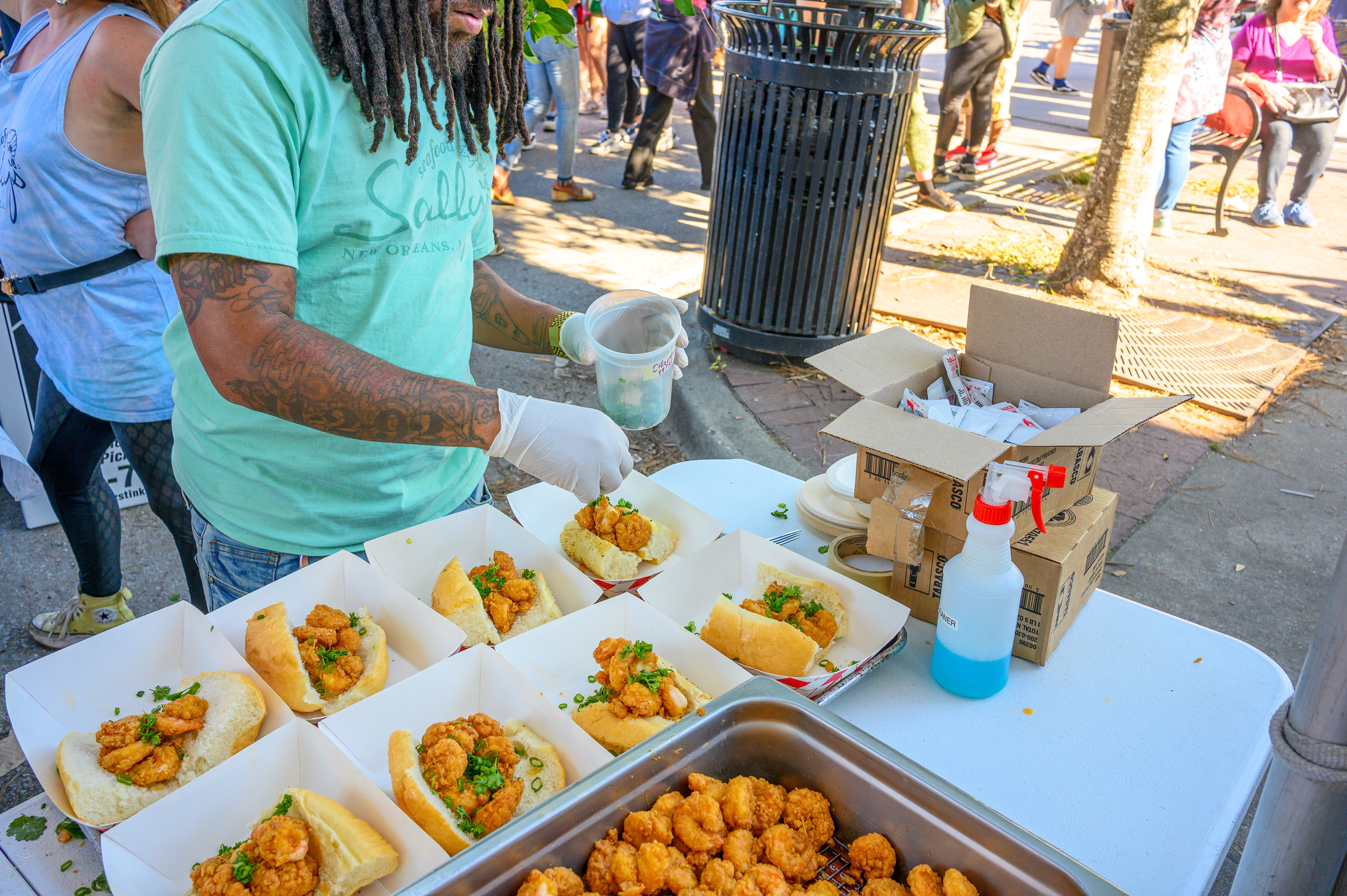 Shutterstock 2391563341 NEW ORLEANS, LA, USA NOVEMBER 19, 2023 Unidentified Worker Sprinkles Cilantro On Shrimp Poboy Sandwiches At The Oak Street Poboy Festival